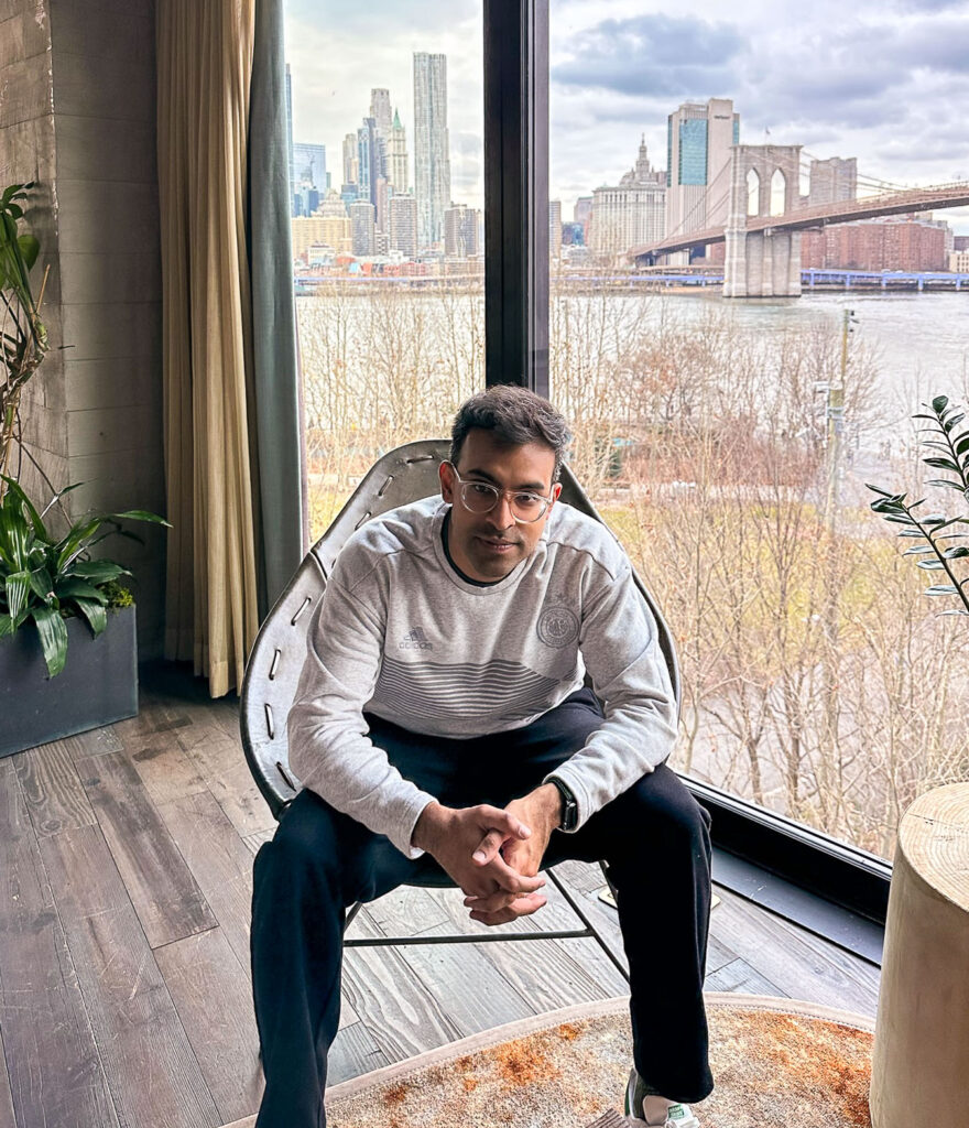 Sanjeev sitting in front of the NYC skyline in the 1 Hotel Brooklyn.
